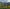 Black drone with yellow accents flying over a scenic landscape with mountains and water.